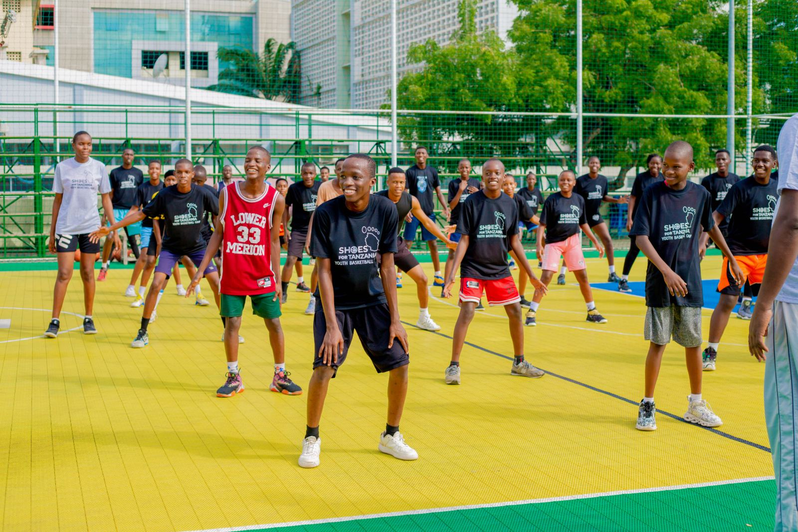 Young athletes in Shoes For Tanzania shirts warming up together on an outdoor court