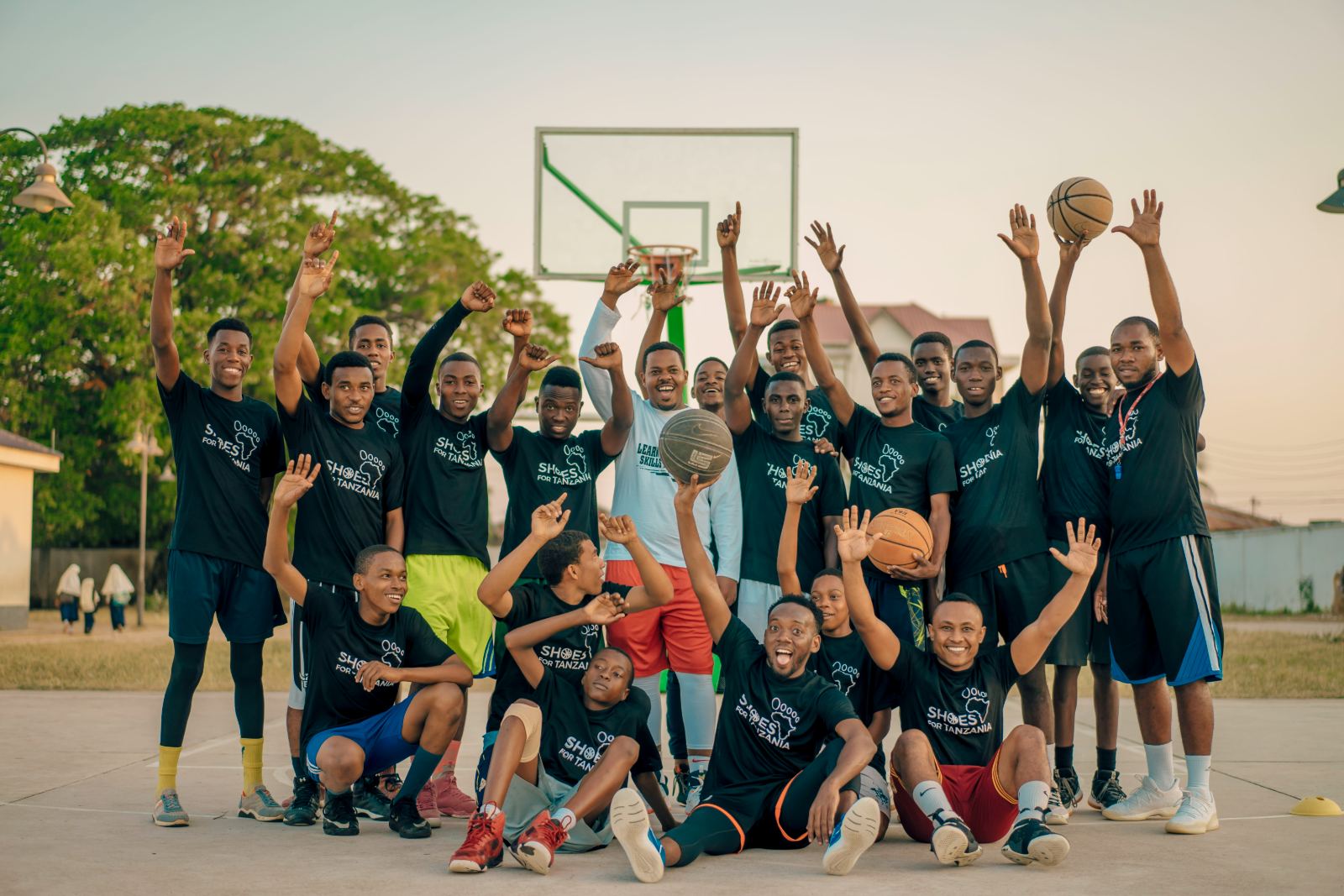 Camp athletes and coaches waving together on an outdoor court at sunset
